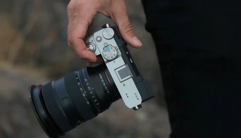 Photographer's hand holding a rangefinder camera with attached telephoto lens.