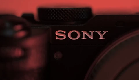 Sony camera body with illuminated branding against warm red ambient lighting.