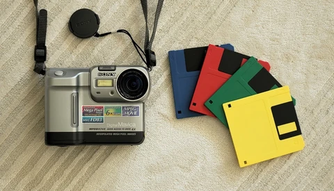 Vintage digital camera with memory cards and lens cap on neutral fabric surface.