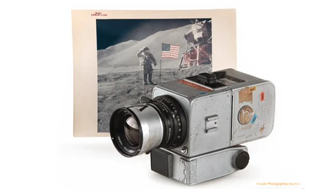 Vintage film camera with telephoto lens displayed alongside a lunar surface photograph featuring an astronaut and American flag.