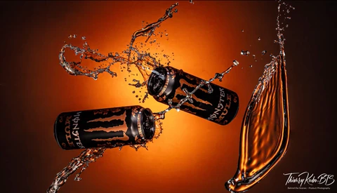 Two beverage cans colliding mid-air with dynamic water splash against warm orange background.