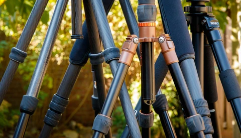 Close-up of multiple tripod legs with adjustment knobs and leather connectors against a blurred green forest background.