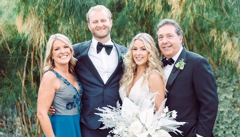 Bride and groom pose with two adults in formal attire against a willow tree backdrop.