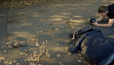 Photographer lying on pavement composing a low-angle shot of a person in blue jacket.