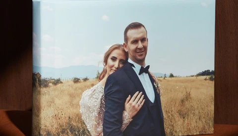 Couple posing in golden field during golden hour with bride's arm around groom's shoulder.