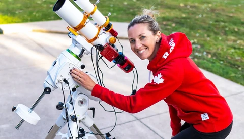 Woman in red jacket posing with a white telescope mounted on an equatorial tracking mount.
