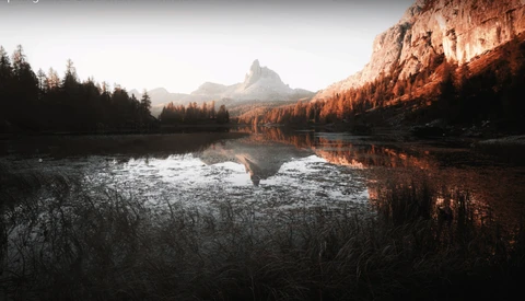 Alpine lake with mirrored reflections of forested peaks and rocky cliffs at golden hour.
