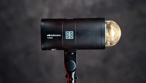 Elinchrom THREE monolight with reflector dome positioned against a dark textured backdrop.