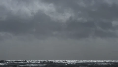 Turbulent ocean waves under heavy gray storm clouds at horizon.