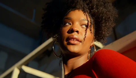Woman with natural curly hair wearing hoop earrings and red clothing, looking upward in dramatic studio lighting.