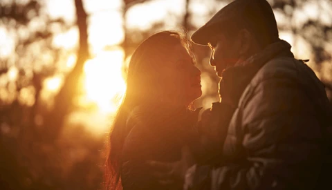 Two people silhouetted against golden sunset light filtering through trees.