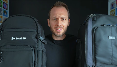 Man standing between two large black camera backpacks against a dark background.