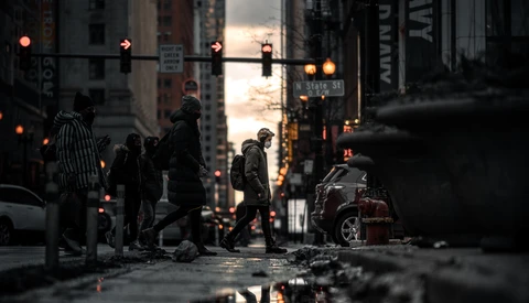 Urban street at dusk with wet pavement reflecting neon signs and city lights.