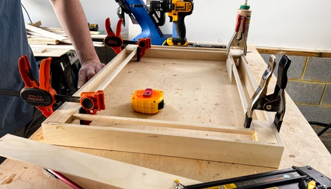 Woodworking workbench with tools, clamps, and a wooden project in progress.