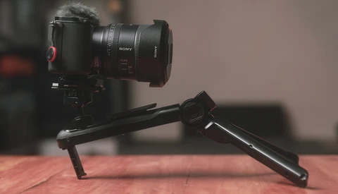 Sony camera with telephoto lens mounted on a black tripod head against a warm-toned backdrop.