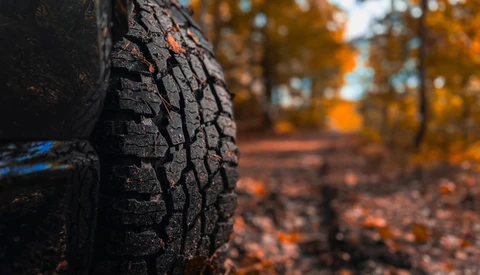 Close-up of a vehicle tire tread with autumn foliage blurred in the background.