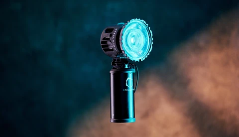 Handheld light fixture with bright cyan LED emission mounted on black handle against blurred background.