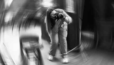 Photographer holding camera to face, captured with radial motion blur effect creating dynamic swirling background.