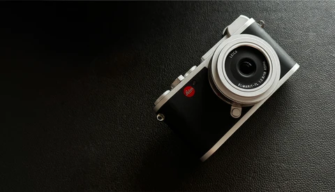 Rangefinder camera with silver top plate and black leather body on dark textured surface.