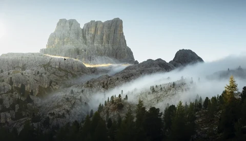 Dramatic mountain peak with columnar rock formations shrouded in rolling mist above a forested valley.