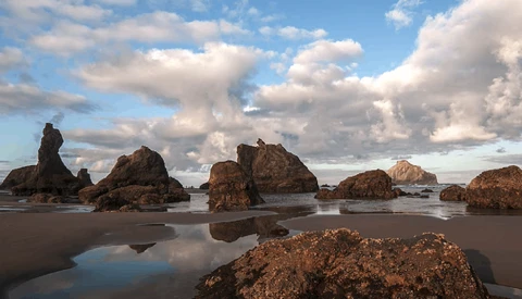 Rocky outcrops and tidal pools on a sandy beach under a dramatic cloudy sky.