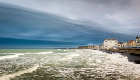 Dramatic coastal town with white-capped waves and moody sky reflected in water.
