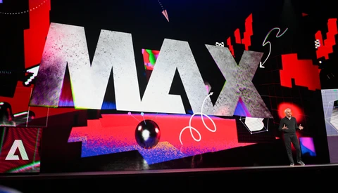 Large-scale conference stage display with bold MAX typography and vibrant neon pink and blue lighting effects.
