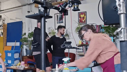 Two people working on a video production set with professional lighting rigs overhead in a creative studio space.