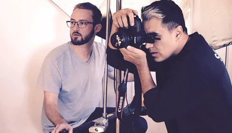 Two photographers examining a Canon camera in a studio setting with white walls and professional lighting.