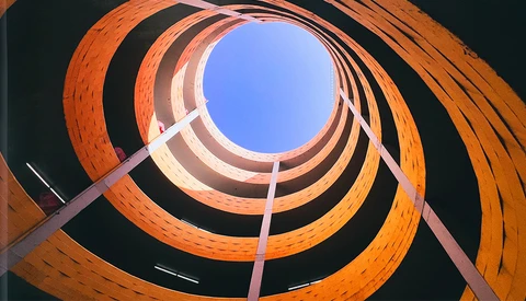 Concentric circles of terracotta brick spiraling upward toward bright blue sky through a cylindrical opening.