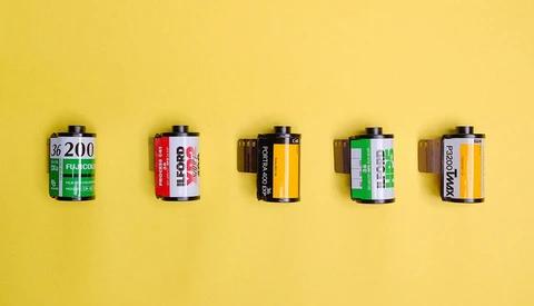 Five vintage film canisters arranged in a row against a bright yellow background.