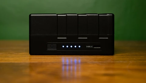 Black USB hub with five glowing blue LED indicator lights mounted on wooden surface against green background.