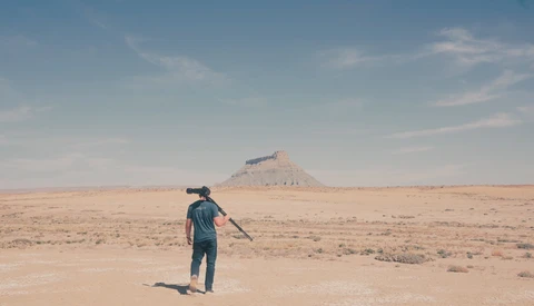 Person standing in vast desert landscape pointing toward distant mountain peak.