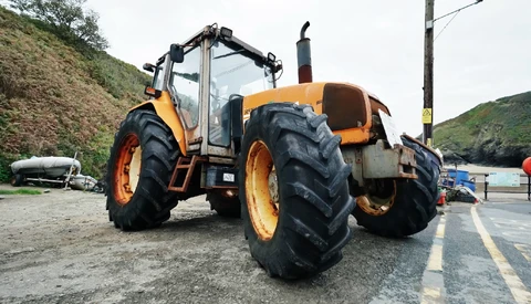 Orange and black heavy machinery tractor with large treaded tires parked on an asphalt road beside a hillside.
