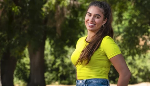 Woman in bright yellow t-shirt smiling at camera with trees in background.