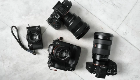 Collection of four black cameras and lenses arranged on a marble surface.