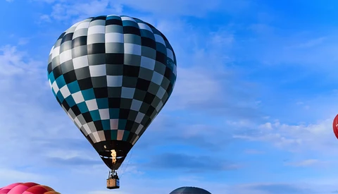 Black and white checkered hot air balloon floating against a blue sky with wispy clouds.