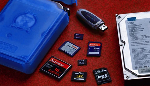 Collection of memory cards and storage devices arranged on red surface next to blue case and external hard drive.