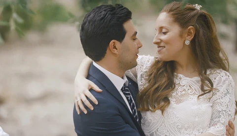 Bride and groom embrace outdoors, bride wearing lace wedding dress and groom in dark suit with striped tie.