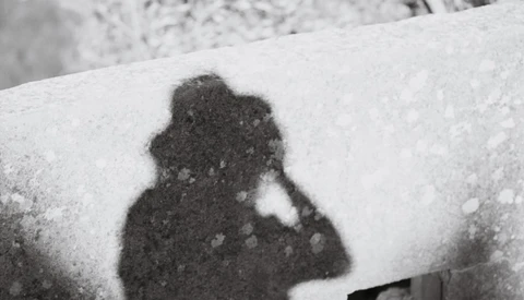 Shadow of a person holding a camera cast on snow-covered surface.