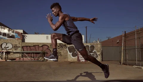 Shirtless male athlete mid-jump in dynamic running pose against urban rooftop backdrop.