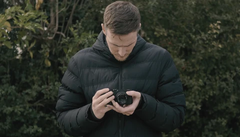 Photographer in black puffer jacket reviewing images on a compact digital camera outdoors.