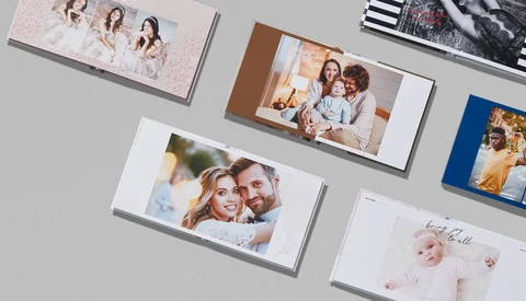 Collection of printed photo books and albums arranged on a gray surface, displaying various family portraits and lifestyle photography.