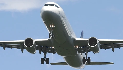Commercial aircraft approaching for landing with landing gear deployed against blue sky.