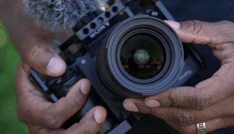 Photographer's hands holding a professional video camera with a wide-angle lens in focus.