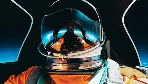 Astronaut in spacesuit with reflective helmet visor showing Earth and spacecraft interior.