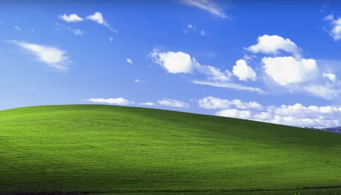 Rolling green hillside beneath blue sky with white cumulus clouds.