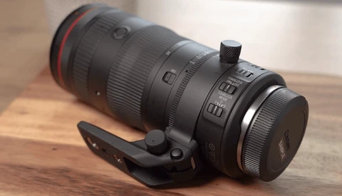 Black telephoto lens with red ring mounted on wooden surface with black camera strap.