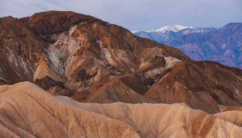 Layered desert mountains with warm earth tones, snow-capped peaks visible in the distance.