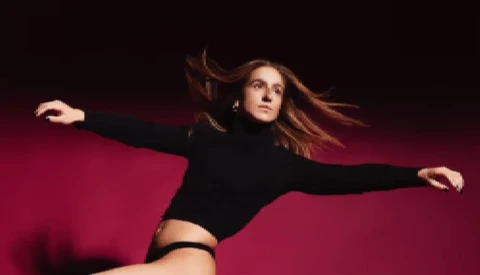 Woman in black crop top and high-waisted bottoms posed dynamically against deep magenta background with arms extended.